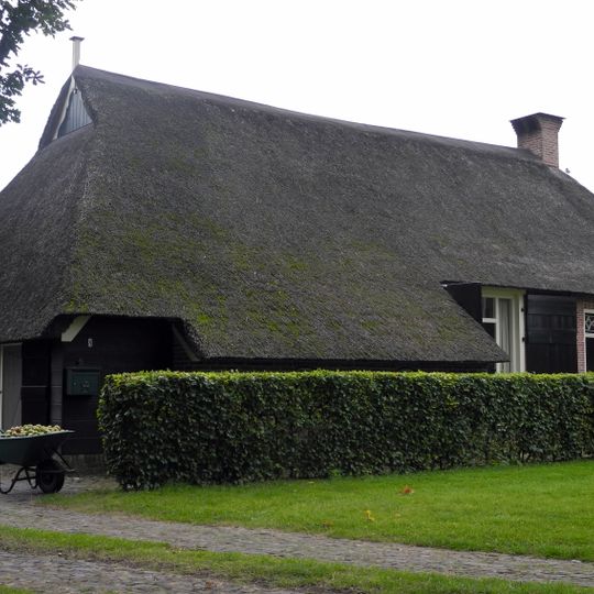 Kleine boerderij met woondeel tegen afgeknotte topgevel onder wolfsdak en met schuurdeel met zijbaander