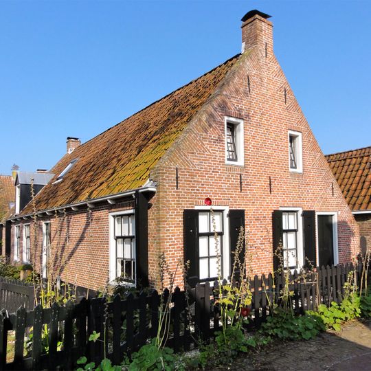 Huis zonder verdieping onder door rode pannen gedekt zadeldak tussen puntgevels met vlechtingen