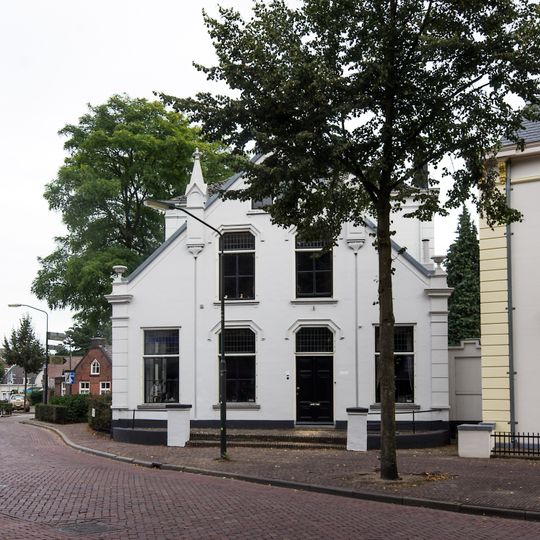 Gepleisterd pand. Het huis bestaat uit een middengedeelte met twee verdiepingen en schilddak, geflankeerd door lage zijvleugels van latere datum, waarvan de zijgevels versierd zijn met pinakels