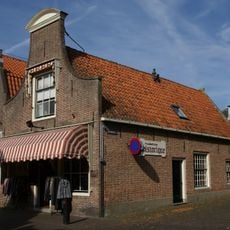 Eenvoudig pand met gezwenkte top aan de westerstraat met oude vensters