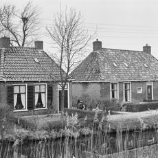 Landelijk pand met goot op klossen onder schilddak met twee hoekschoorstenen