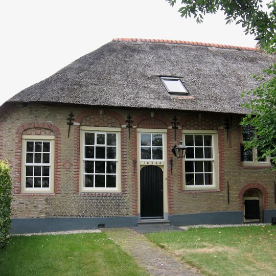 Boerderij onder rieten wolfdak, evenwijdig aan de straat gebouwd. Geblokte ontlastingsbogen en sierankers; vensters met twaalf- en negenruitsschuiframen.