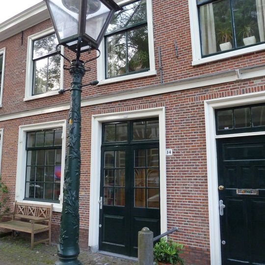 Laag huis met rechte kroonlijst, beneden intact, hier enige schuiframen met oude roeden en luiken. Stoep met palen