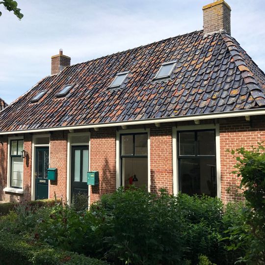 Breed landelijk pand met goot op klossen onder schilddak met twee hoekschoorstenen