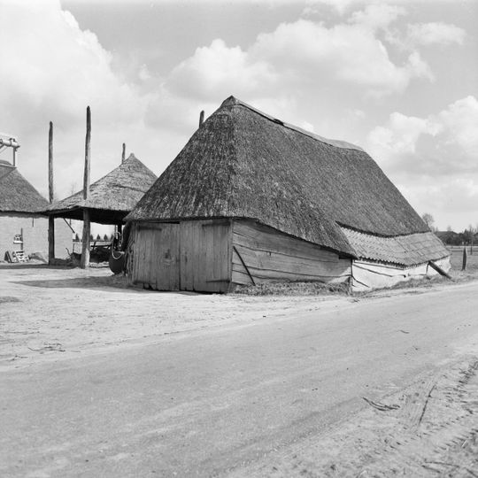 Houten schaapskooischuur. Inrit met kopgevel, met riet gedekt schilddak. In de zijgevel gedeeltelijk gedekt met pannen