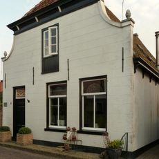 Pand met ingezwenkte witte gevel onder afgewolfd zadeldak