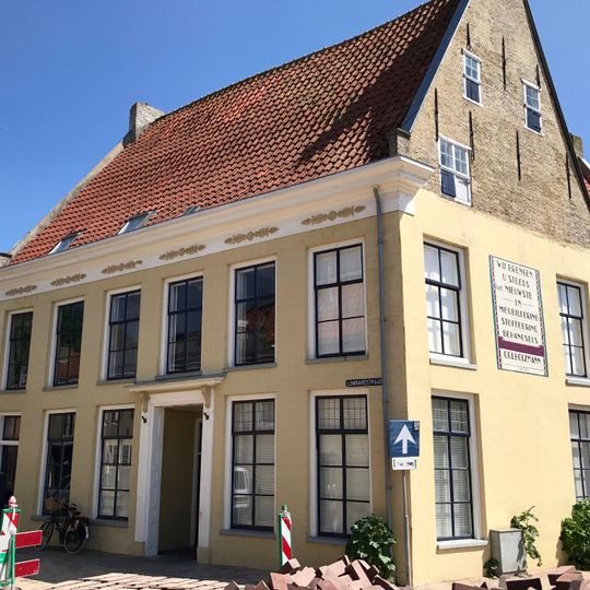 Groot L-vormig met tuitgevels en kloostervensters in de top en kroonlijst met opgelegde decoratieve ornamenten