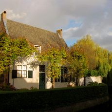 Eenvoudige gepleisterde lage woning met zadeldak, de korte zijden in topgevels eindigend. Terzijde uitgebouwde schoorsteen