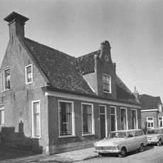 Groot dorpshuis met ingang met Vlaamse top onder zadeldak tussen topgevels waarop hoekschoorstenen met borden (vormt een geheel met nr. 32)