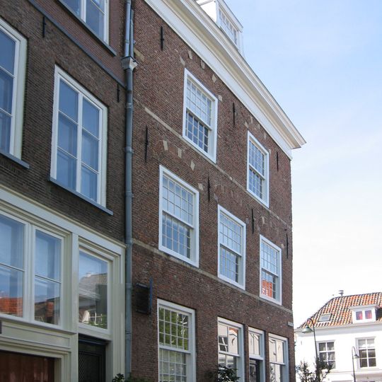 Hoekpand met hoog schilddak, dat aan de achterzijde wordt afgesloten door een puntgevel. Gepleisterde gevels met rechte kroonlijsten