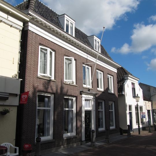 Herenhuis met verdieping ter breedte van vijf vensterassen. Rijk gesneden deur in een omlijsting door pilasters, die een hoofdgestel met snijwerk dragen. Drie stoeppalen
