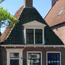 Laag pandje onder hoog schilddak waarop topschoorsteen met bord