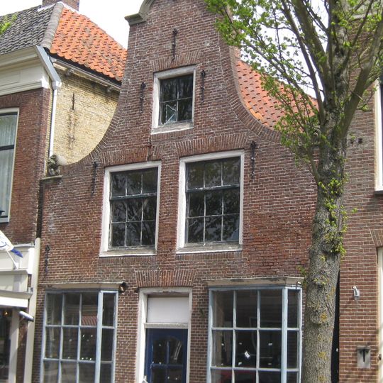 Pand met gerestaureerde vensters en pui onder zadeldak tegen klokgevel met aanzetkrullen en kuifstuk