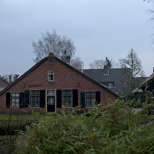 Boerderij, langhuis, zijbaander, rieten dak met plaggen op de nok. Achter op het erf, aan de zijde van Boekweitskorrel, een vrijstaande hooiberg met vijf houten roeden en een rietgedekte sporenkap