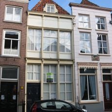 Huis onder schilddak en met lijstgevel die door gegroefde verticale stijlen ingedeeld is waartussen de vensters terugliggen