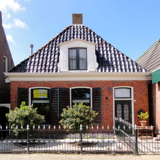 Pand zonder verdieping tegen gevels met houten gootlijst onder hoog schilddak met dakkapellen en topschoorstenen