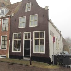 Hoekpand met klokgevel onder diep zadeldak met iets hoger opgetrokken achterhuis