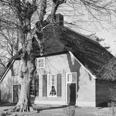 Hoeve onder rieten wolfdak. De voorgevel bezit vlechtingen en vensters met luiken en 18-ruitsschuiframen. Stal met gepotdekselde houten delen