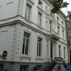 Dubbel hoekpand, gebouwd in 1685, geheel verbouwd in 1860/61 door cornelis outshoorn, met van rijke stucversieringen voorziene gepleisterde gevels onder bewerkte lijst, en zandstenen pui met balcon