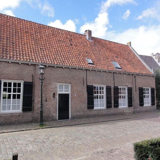 Eenvoudig huis met zadeldak tussen zijtopgevels met vlechtingen ramen met kleine roedenverdeling, houten klossen onder de gootlijst, vensterluiken, rode pannen