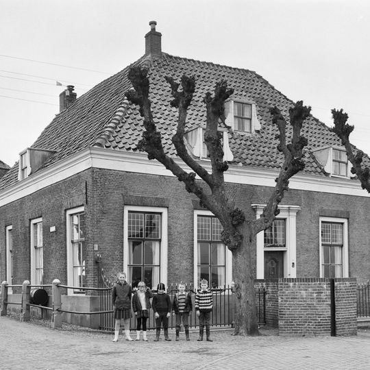 Op de hoek van de Westdijk gelegen pand zonder verdieping onder omlopend pannen schilddak, waarin dakvensters met zijstukken.