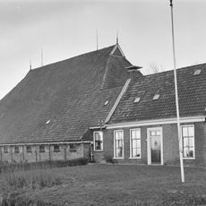Kop-hals-rompboerderij met voorhuis tussen topgevels met boeiborden, omlijste ingang, zesruitsvensters en topschoorstenen met borden