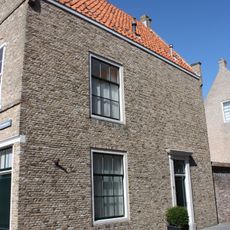 Pand met in schoon metselwerk uitgevoerde trapgevel met topbekroning, de treden afgedekt met natuurstenen platen