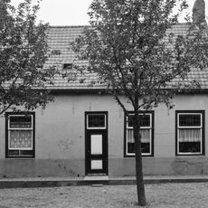 Dwarshuis met onregelmatig ingedeelde gepleisterde gevel aan het plein