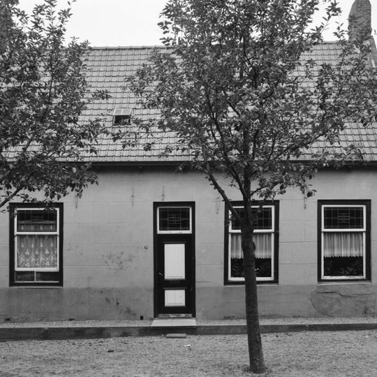 Dwarshuis met onregelmatig ingedeelde gepleisterde gevel aan het plein