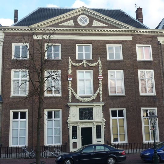 Pand met brede bakstenen gevel, fronton en klassieke gootlijst, gebeeldhouwde natuurstenen ingangspartij. Hardstenen stoep, ijzeren hek