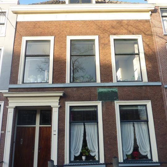 Pand met brede bakstenen gevel. Ingangspartij met omlijsting. Hardstenen stoep met stoeppalen