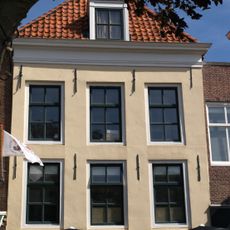 Huis met gepleisterde lijstgevel. Dakkapel. Moderne winkelpui