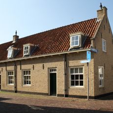 Pand met wit gepleisterde gevel en houten consoles onder de lijst