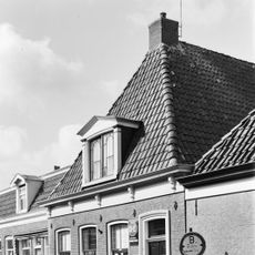 Pand met onlijste ingang en gesneden consoles aan de kroonlijst onder hoog zadeldak met voorschild met versierde dakkapel en topschoorsteen