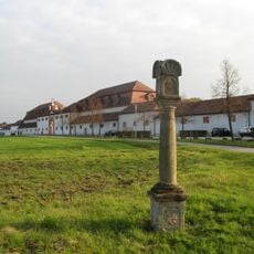 Hochrechteckiger Sockel mit verzierten Katuschen; Säule unten und oben mit Ringwulst; Doppelkapitell mit Voluten; Laterne mit vier leeren Bildnischen; Kreuzförmige Bedachung, darin Muschel-Relief.