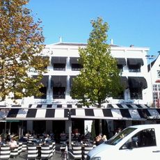 Dubbelpand met gemeenschappelijke, wit gepleisterde lijstgevel van zes traveeën breed en langs de voorgevel een stoep met smeedijzeren stoephekken