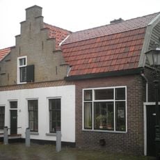 Pand onder zadeldak tegen trapgevel boven geblokt fries en langs de treden rode klesoren