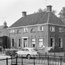 Pand met omlijste ingang en verdieping onder schilddak met hoekschoorstenen en gedichte halfronde lichtopeningen (mog. kaaspakhuis)