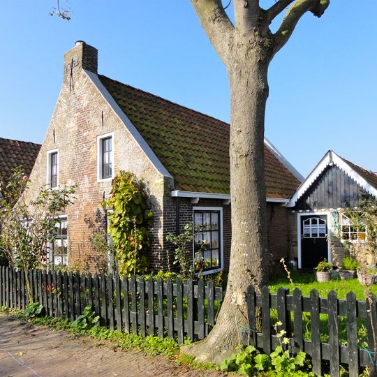 Huis zonder verdieping onder door rode pannen gedekt zadeldak tussen puntgevels met vlechtingen