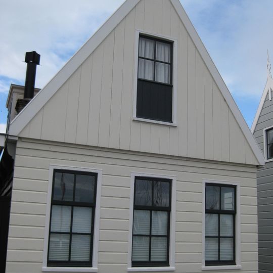 Houten huis met skelet. Puntvormig voorschot, goede pui en roedenverdeling. Gepotdekselde achtergevel met goede roedenverdeling in de vensters en een deurtje uit derde kwart 18e eeuw