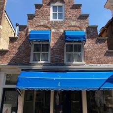 Pand onder zadeldak tussen topgevel achter en gepleisterde trapgevel met verdiepte vensternissen voor