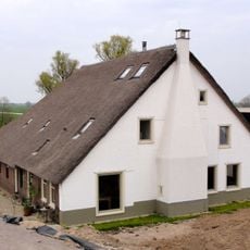 Gepleisterde hoeve, rieten wolfdak en links uitgebouwde vleugel onder zadeldak, afgesloten door een puntgevel met rookkanaal in de as. Bakhuis