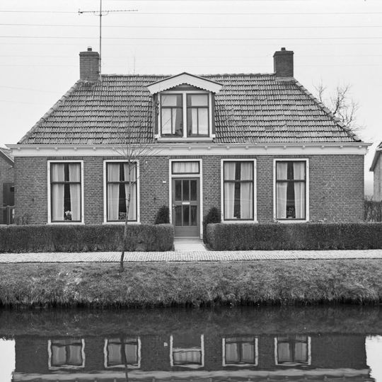 Dubbel landelijk pand met goot op klossen onder schilddak met dakkapel en twee hoekschoorstenen