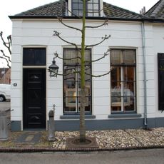 Pand met gepleisterde gevel. Goede vensters en deur. Stoeppaal met kettingen. Keitjesstoep, lindeboom