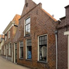 Pand met gewijzigde vensters in topgevel met vlechtingen, waterlijst en toppinakel op natuurstenen consoles