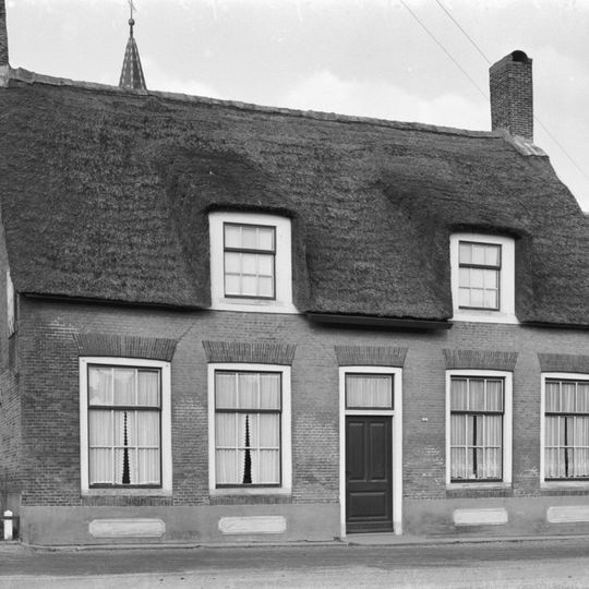 Fraai geproportioneerd woonhuis van een boerderij van begane-grond met hoog, rieten zadeldak tussen puntgevels met topschoorstenen en met twee dakvensters onder opgewipte dakgedeelten