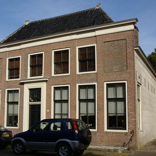 Pand met brede gevel met hoekpilasters en middenrisaliet; stoep met marmeren tegels. Tuinkoepel aan de Hoogstraat. Tuighuis langs zijmuur van de tuin