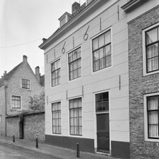 Huis met gepleisterde lijstgevel voorzien van twee dakkapellen en jaartalankers. Rozet bovenlicht