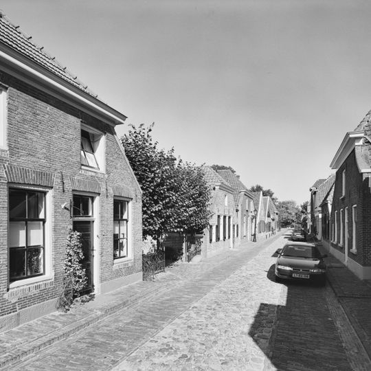 Pand onder een aan de achterzijde afgewolfd zadeldak. Voorgevel met houten topschild en zesruitsschuifvensters, met luiken behangen. ''De Tapperijen van de Steensteeg''