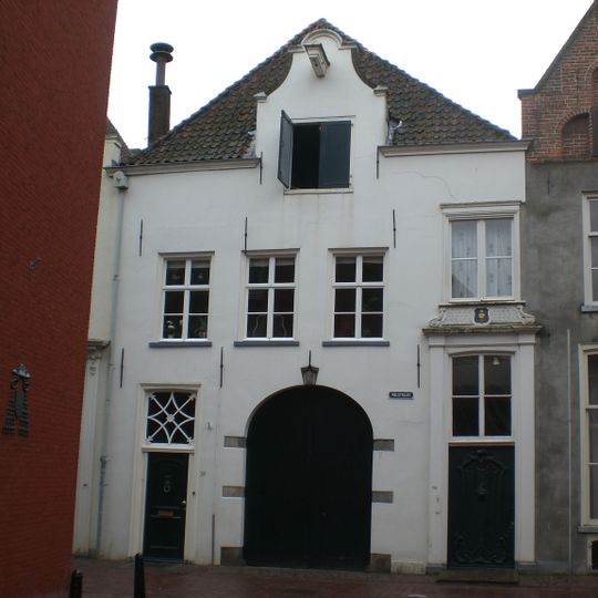 Breed pand met gepleisterde rechte gevel, in het midden een klokvormig verhoogd gedeelte, waarin hijsbalk en pakhuisluik